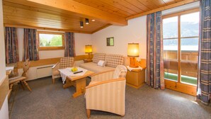 A cozy room with a wooden ceiling, a checkered sofa, a small table with a lamp, and a view of the outdoors through a window.