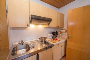 A kitchen with wooden cabinets, a stainless steel sink, a kettle, and a coffee maker.