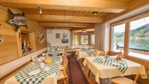 A wooden cabin with checkered tablecloths, wooden chairs, and a view of a lake.