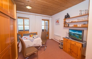 A cozy room with a dining table set for two, a television on a wooden cabinet, and a window with a view of a lake.