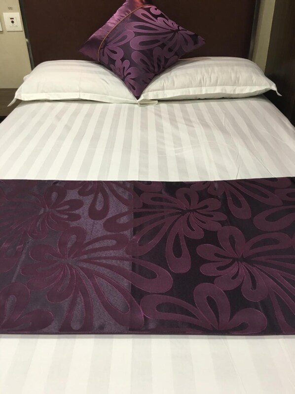 A bed with striped bedding and a purple floral bedspread.