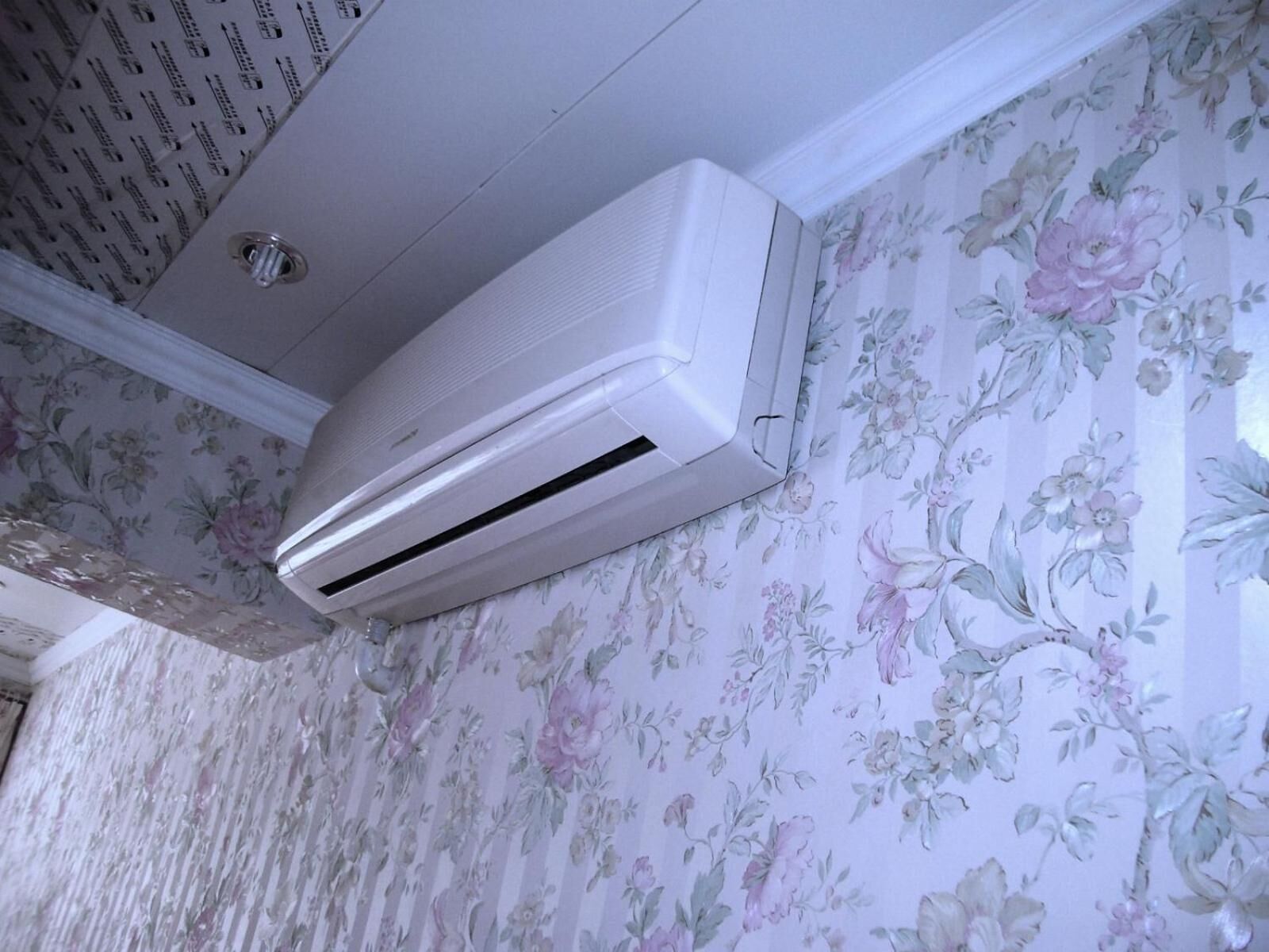 An air conditioning unit mounted on a wall with floral wallpaper.