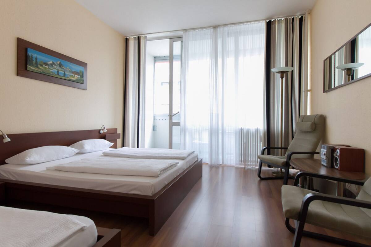 Una habitación de hotel con una cama grande, un escritorio con una silla, una lámpara y un cuadro en la pared.