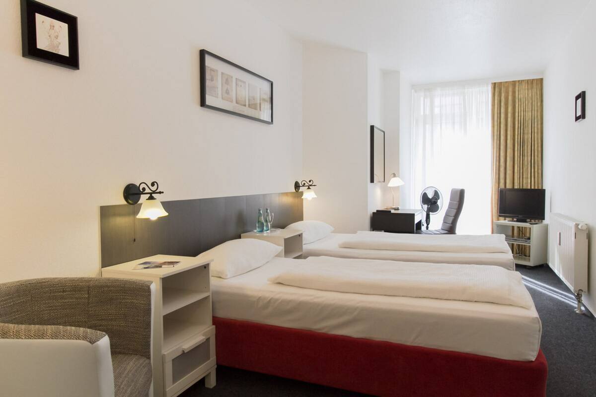 Habitación de hotel con dos camas, un escritorio, una silla, un televisor y una ventana con cortinas.