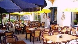 An outdoor cafe with wooden tables and chairs, umbrellas providing shade, and a child standing near the entrance. - Hotel Gasthaus Café Bavaria (Inzell)