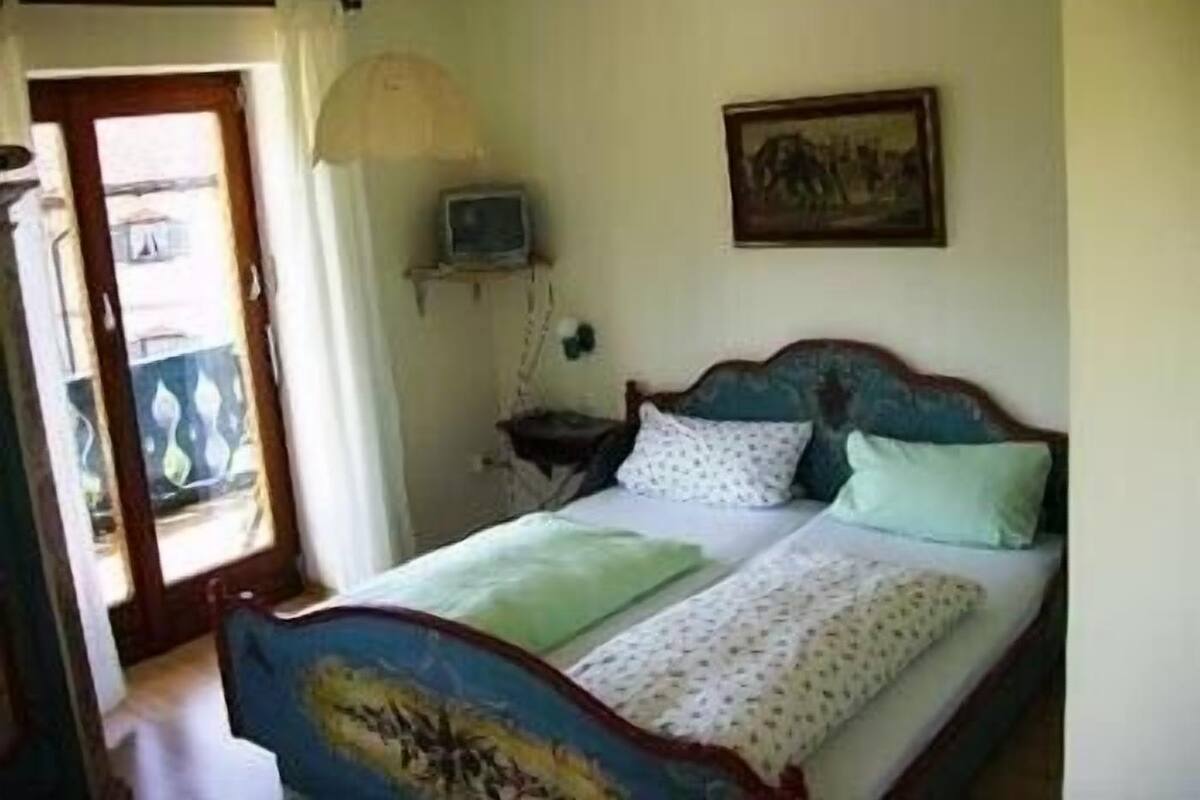 Een slaapkamer met een bed, een klein nachtkastje, een aan de muur bevestigde televisie en een deur die leidt naar een buitenruimte.
