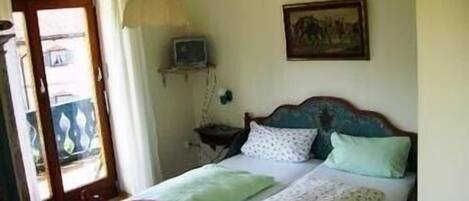 Un dormitorio con una cama, una mesita de noche, un televisor montado en la pared y una puerta que da a un espacio al aire libre.