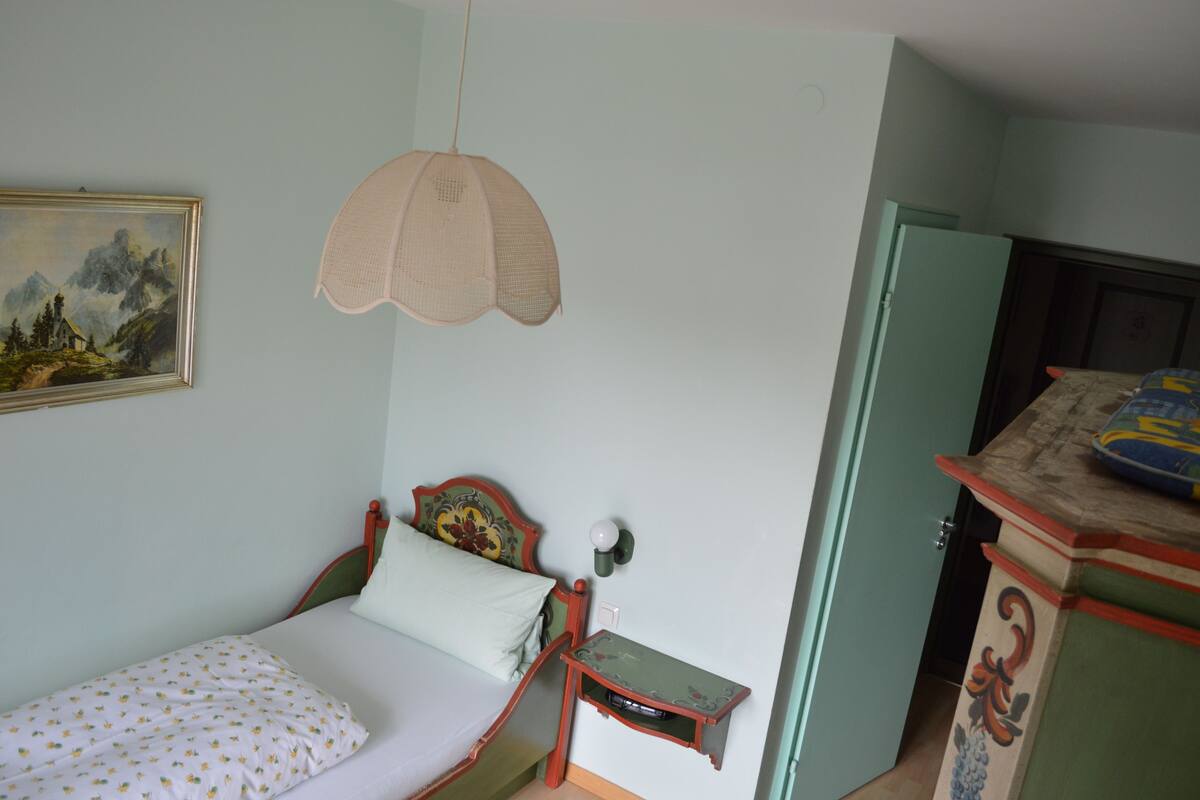 Een slaapkamer met een eenpersoonsbed, nachtkastje, lamp, dressoir en een schilderij aan de muur.