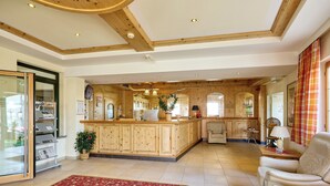 Un hall d’entrée spacieux avec un comptoir d’accueil en bois, une moquette rouge à motifs et un coin salon comprenant un canapé et des fauteuils.