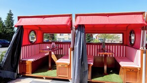 Une résidence mobile aux rayures rouges et blanches, avec une petite table et un espace détente composé d’un banc.