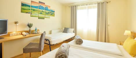 Ein Hotelzimmer mit zwei Betten, einem Schreibtisch mit Computer, einem Stuhl und einem Fernseher.