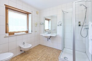 A bathroom with a toilet, two sinks, a shower, and a window with a curtain. - Airport-Hotel Fortuna (Lautzenhausen)