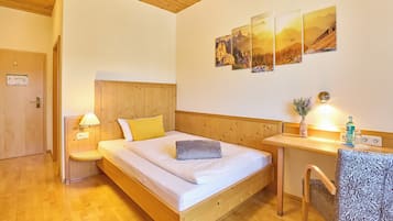 Un lit en bois avec une tête de lit, une table de chevet avec une lampe et une chaise recouverte d’un tissu à motifs. Trois tableaux encadrés sont accrochés au mur.