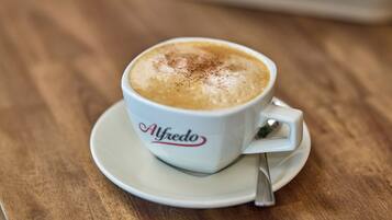 A cup of coffee with a spoon on a saucer, labeled "Alfredo," on a wooden table.