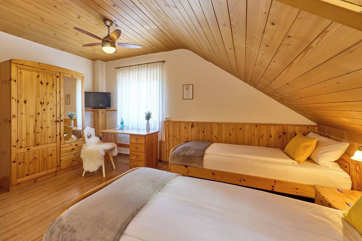 Una habitación acogedora con techo de madera, una cama, un escritorio con silla, un armario y un televisor.