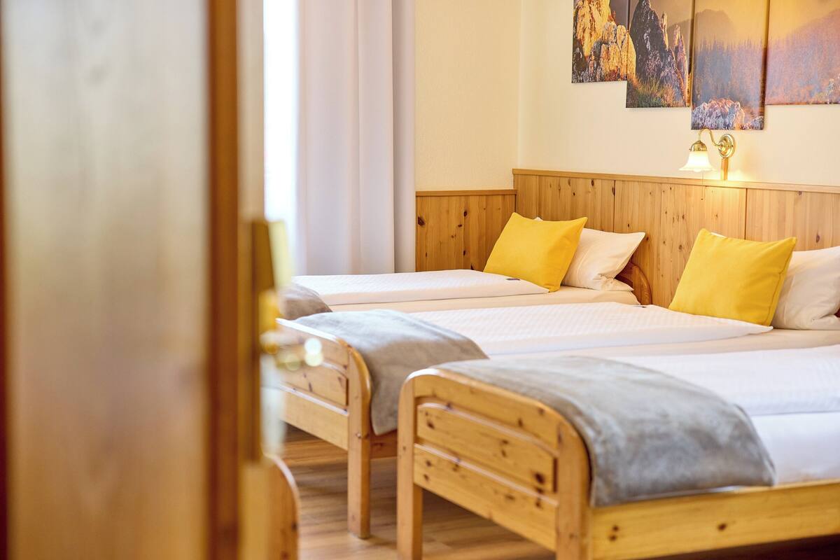 Habitación de hotel con dos camas de madera, cada una con un cojín blanco y uno amarillo.