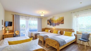 Une chambre d’hôtel avec trois lits en bois, un bureau avec un ordinateur, une chaise et un téléviseur.