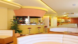 A lobby with a curved seating area, a bar with stools, and a reception desk. - Hotel Oasis (Alghero)