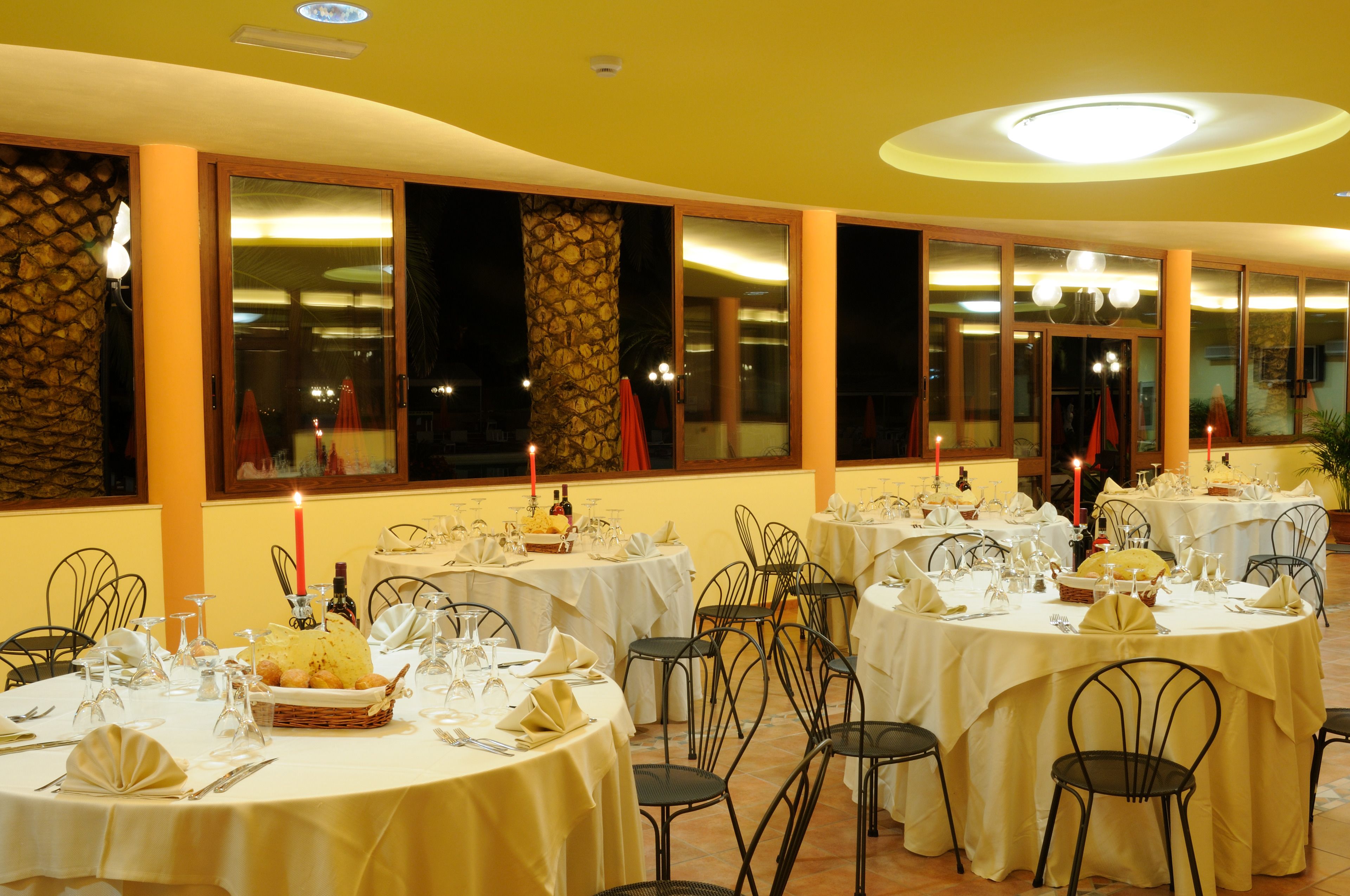 A restaurant with multiple round tables set for dining, featuring white tablecloths and candle centerpieces.