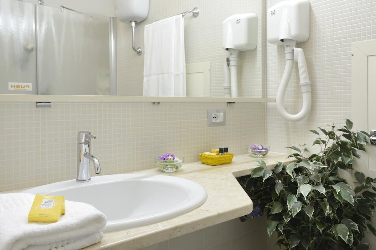 A bathroom with a sink, a mirror, a towel rack, a hand dryer, and a potted plant.
