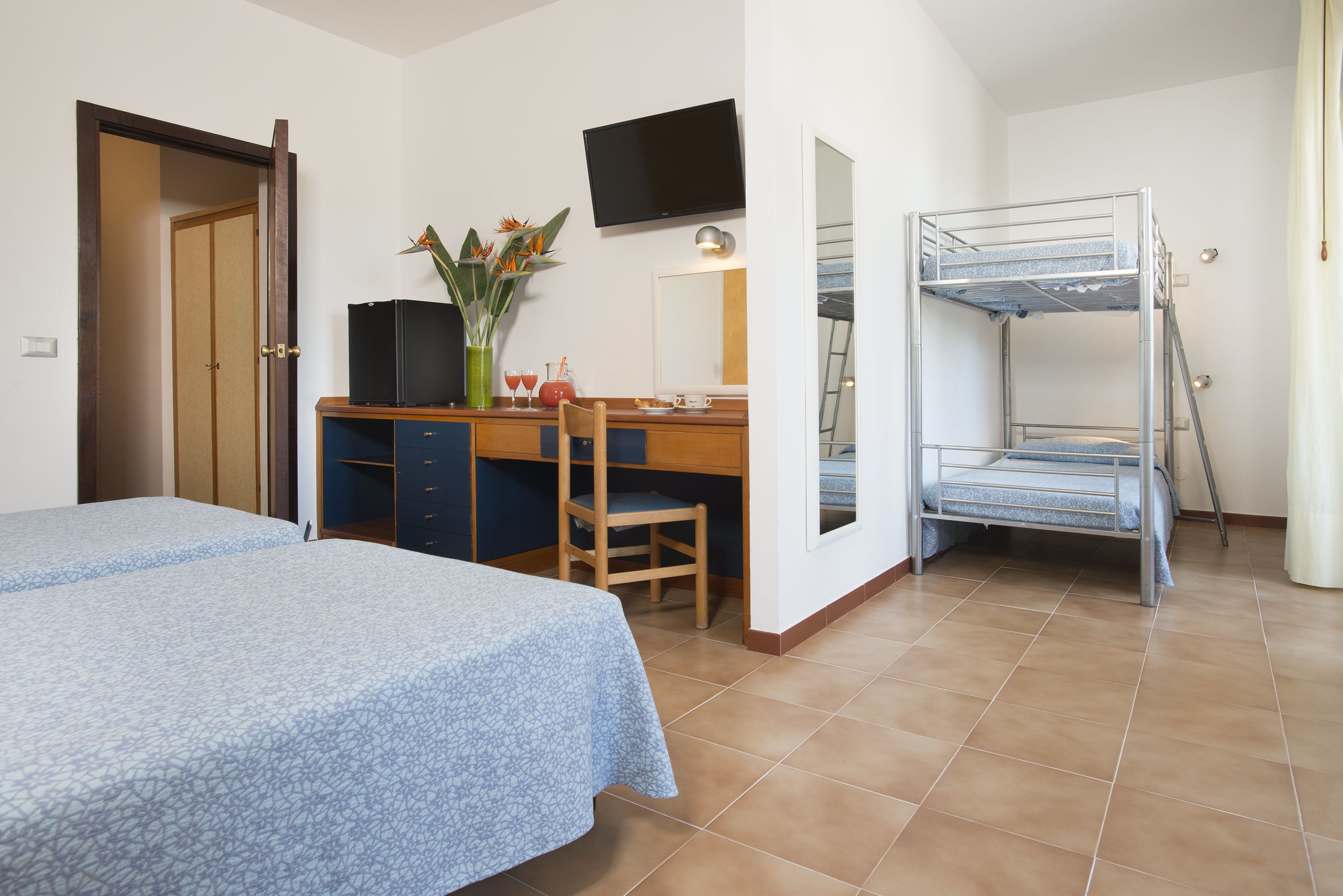 Ein Schlafzimmer mit Etagenbett, Schreibtisch mit Stuhl, Fernseher und einem Bett mit blauen Bettbezug.