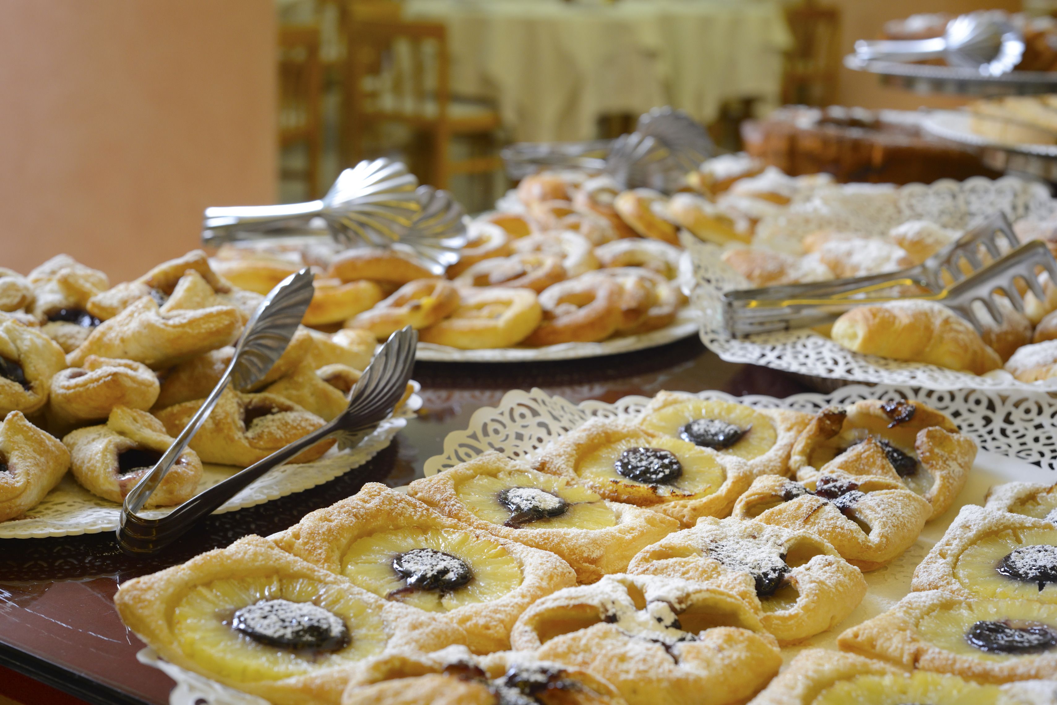 En buffetbord med forskellige kager og desserter, herunder tærter og flødekager, anrettet på tallerkener og fade.