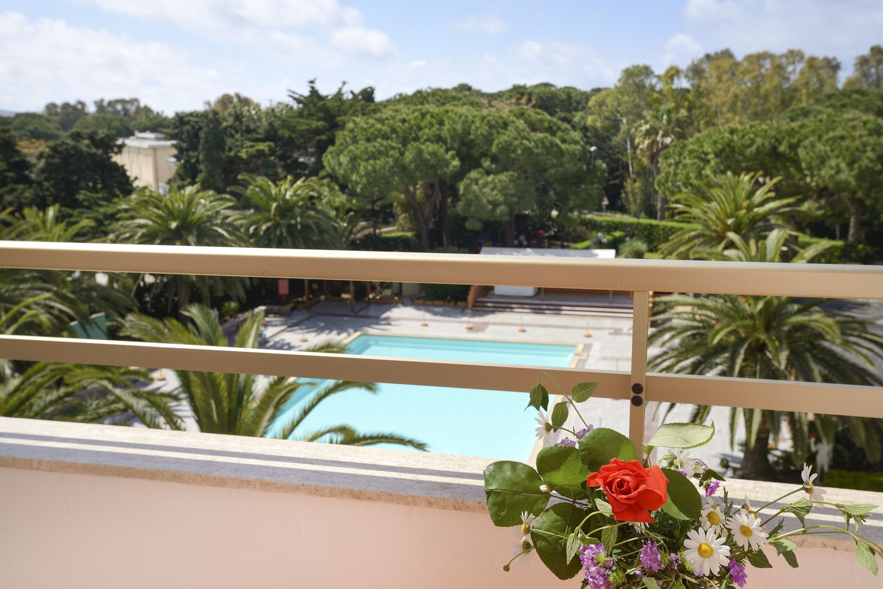A balcony with a view of a swimming pool, surrounded by lush greenery and palm trees.