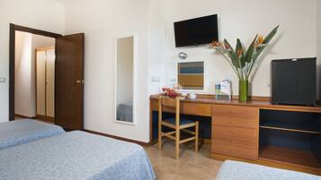 Une chambre d’hôtel avec deux lits, un bureau avec une chaise, une télévision, un miroir et une plante.