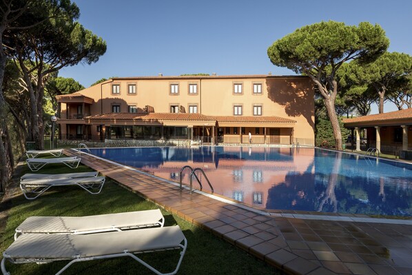 A swimming pool with lounge chairs, a building with multiple windows, and trees in the background.