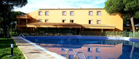 Una piscina con un borde de baldosas, una escalera metálica y un edificio con varias ventanas al fondo.