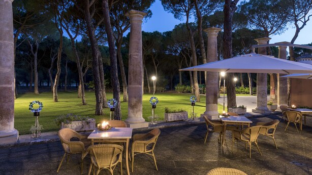 An outdoor patio area with wicker furniture, stone columns, and a well-lit ambiance.