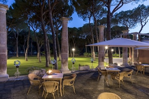 An outdoor patio area with wicker furniture, stone columns, and a well-lit ambiance.