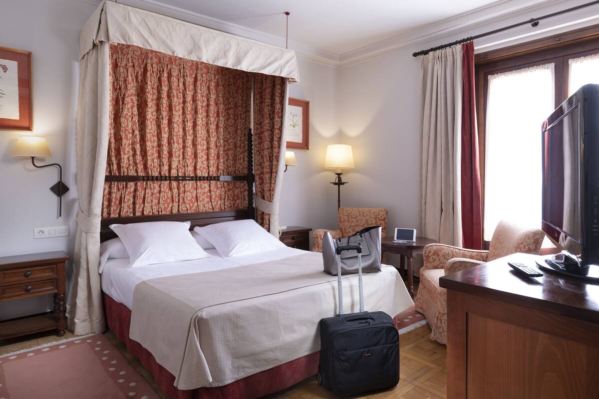 Een hotelkamer met een hemelbed, een bureau met een computer, een stoel en een televisie.