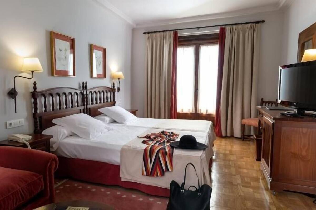 Een hotelkamer met een bed, een bureau met een televisie, een rode fauteuil en twee wandlampen.