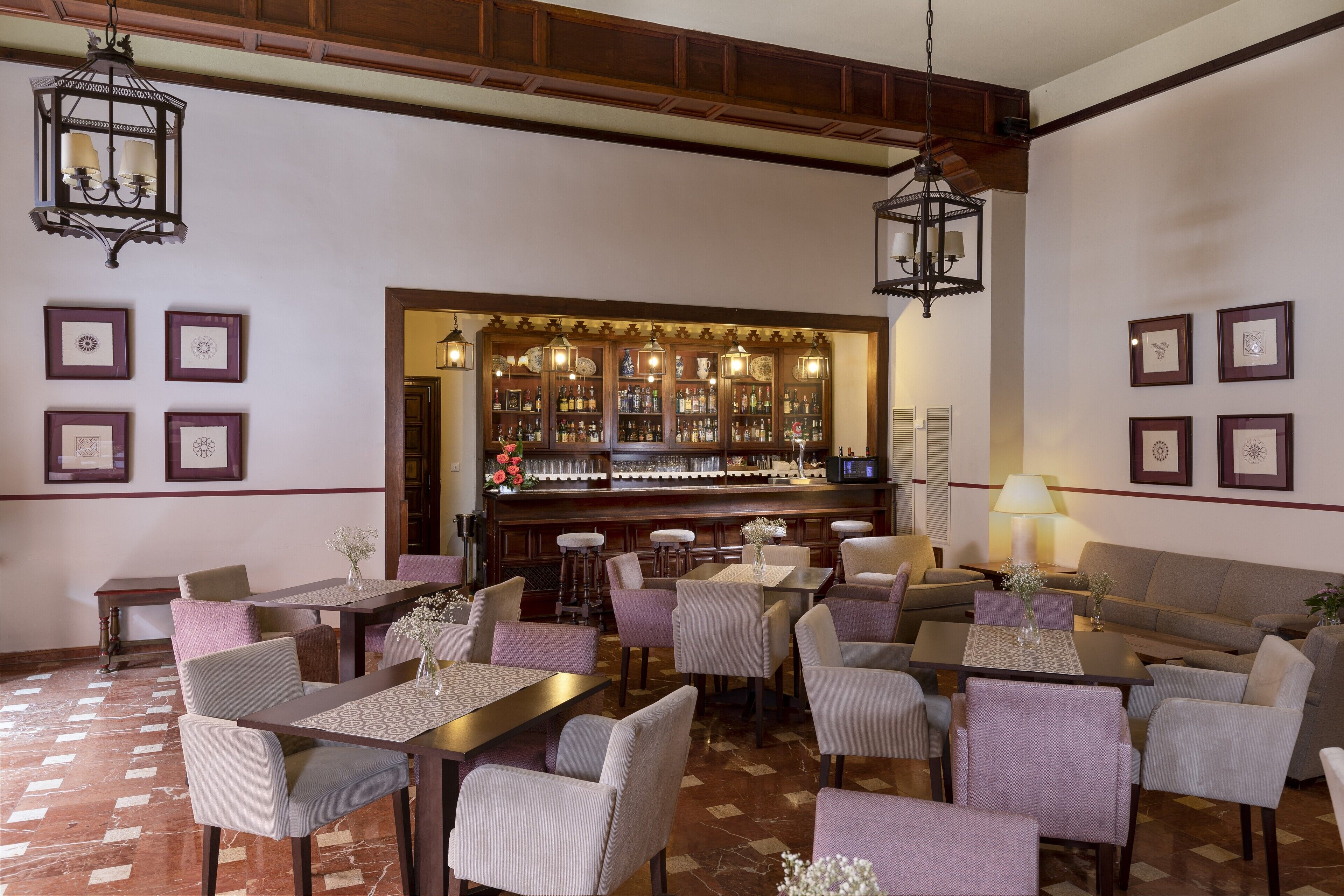 Un restaurante con varias mesas y sillas, una zona de bar con estantes llenos de botellas y cuadros en las paredes.