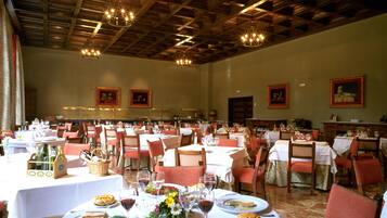 Un amplio comedor con varias mesas dispuestas para una comida, que cuenta con un alto techo con vigas de madera y candelabros.