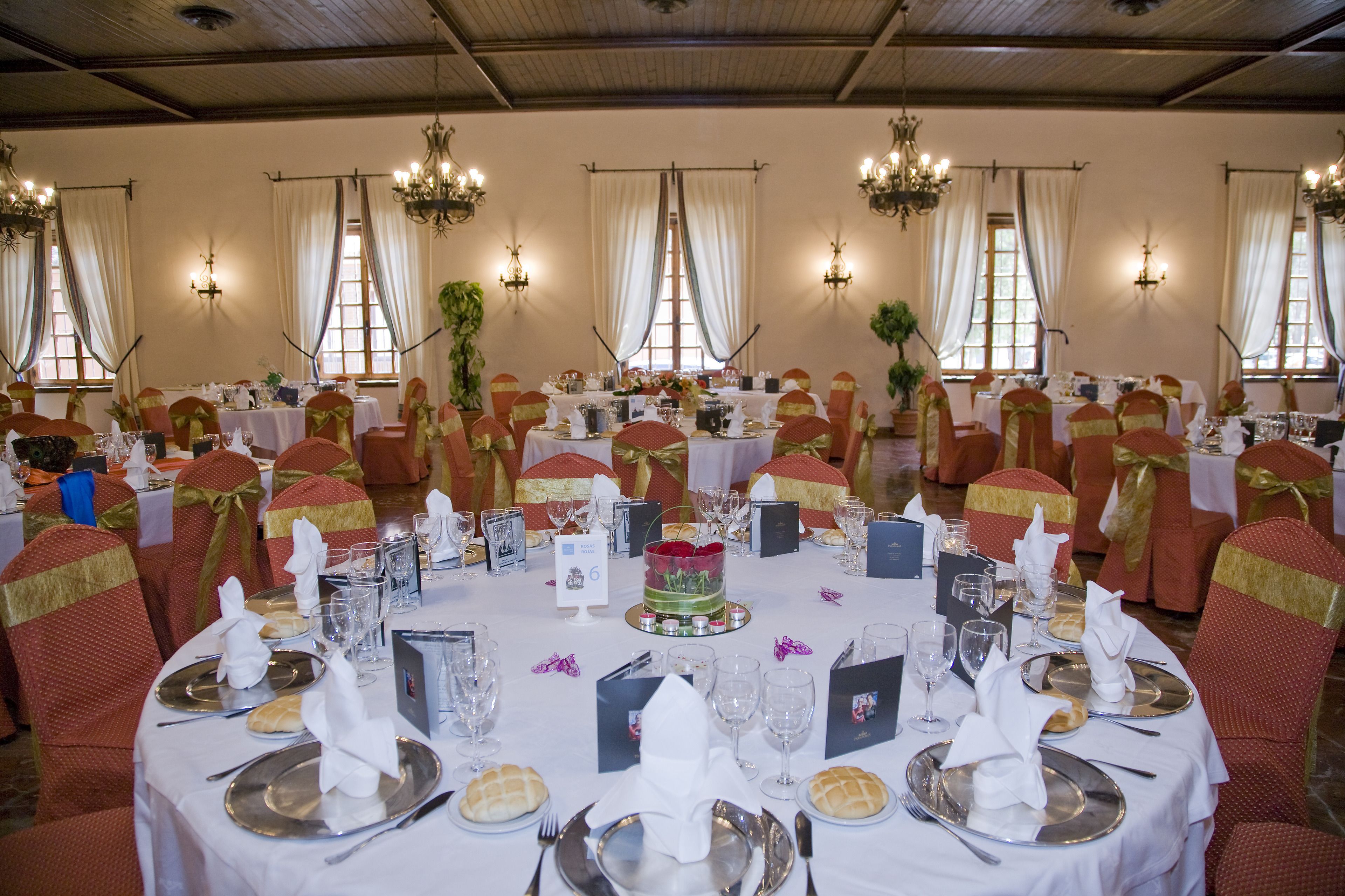 Une salle de banquet avec des tables rondes dressées pour un événement formel, agrémentées de nappes blanches, de rubans dorés et de décorations de table élégantes.