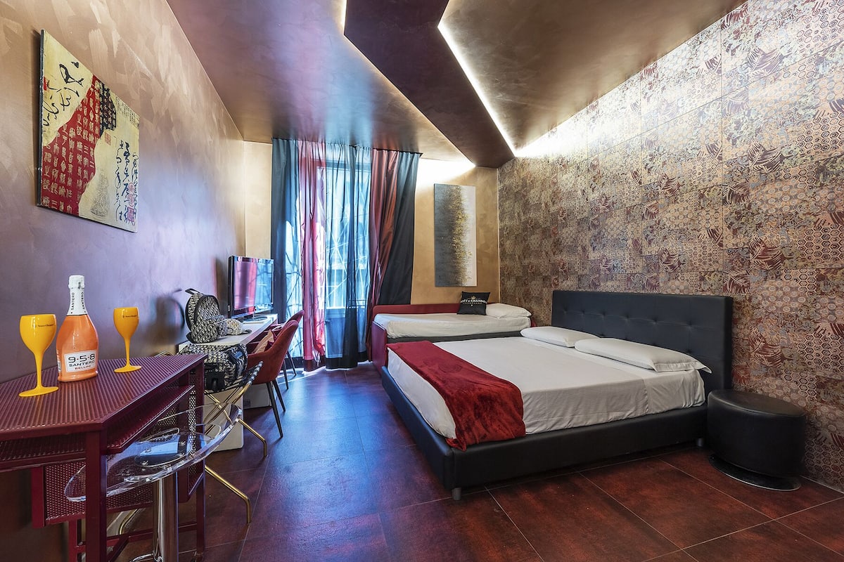 A hotel room with a bed, a desk with a chair, a TV, and a large window with curtains.