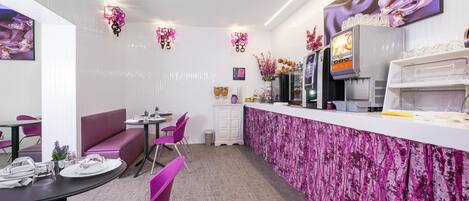 A restaurant with a pink floral theme, including a counter, seating area, and decorative wall art.