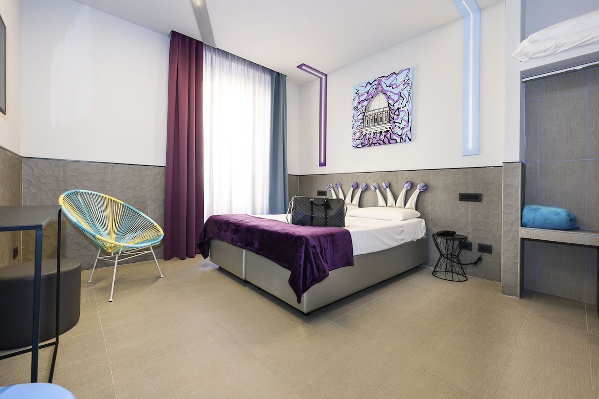 A modern hotel room with a bed, a chair, a small table, and a bathroom area.