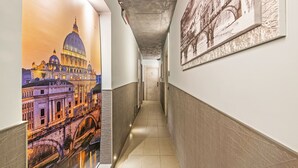 Un couloir orné d’une fresque représentant un paysage urbain, doté d’un sol carrelé et d’un plafond sobre.