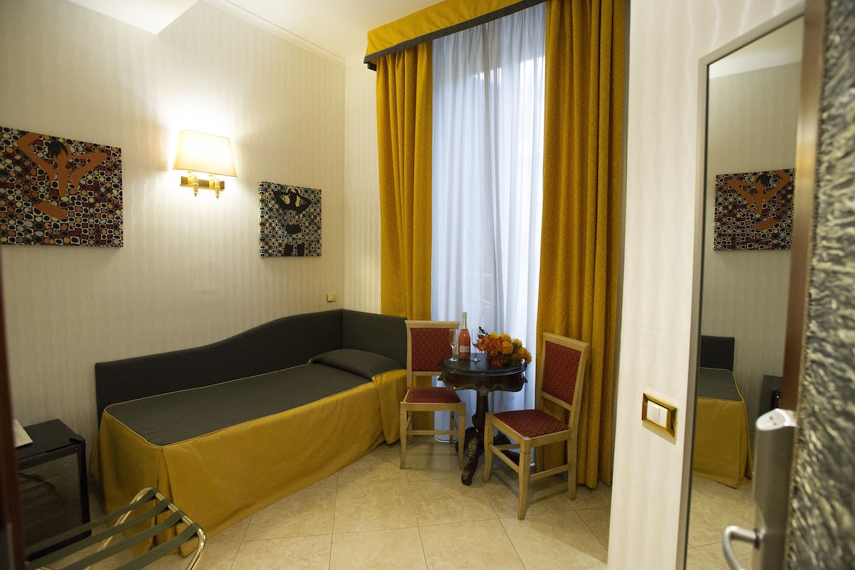 A compact hotel room with a bed, a small table with chairs, and artwork on the walls.