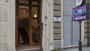 L’entrée d’un hôtel, avec un escalier menant à l’intérieur, une horloge et une enseigne indiquant le nom de l’hôtel.