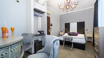 A compact hotel room with a bed, bedside tables, a chair, a desk, and a chandelier.