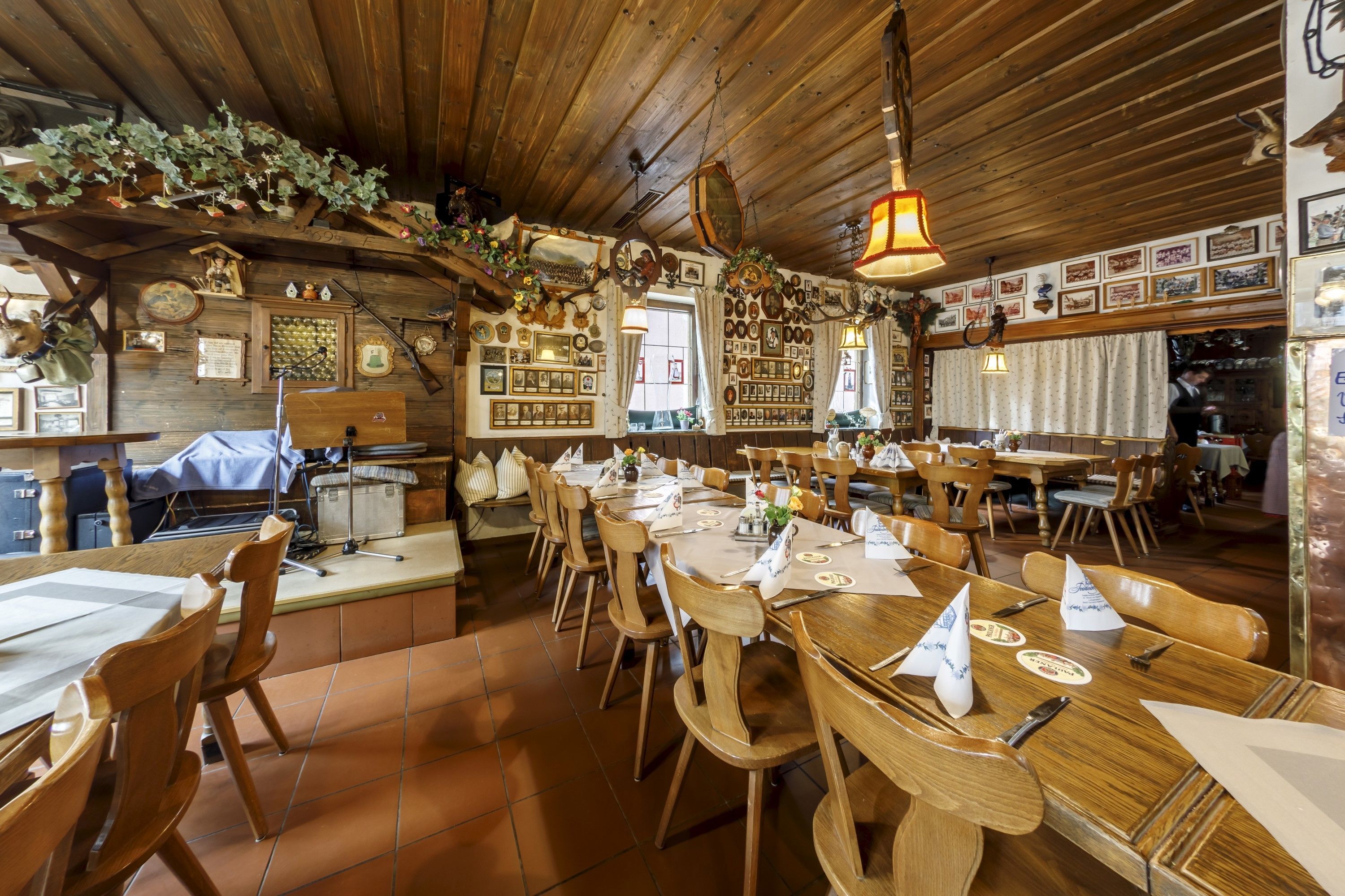 Uma sala de jantar rústica com mesas e cadeiras de madeira, diversas fotos emolduradas nas paredes e um lustre.