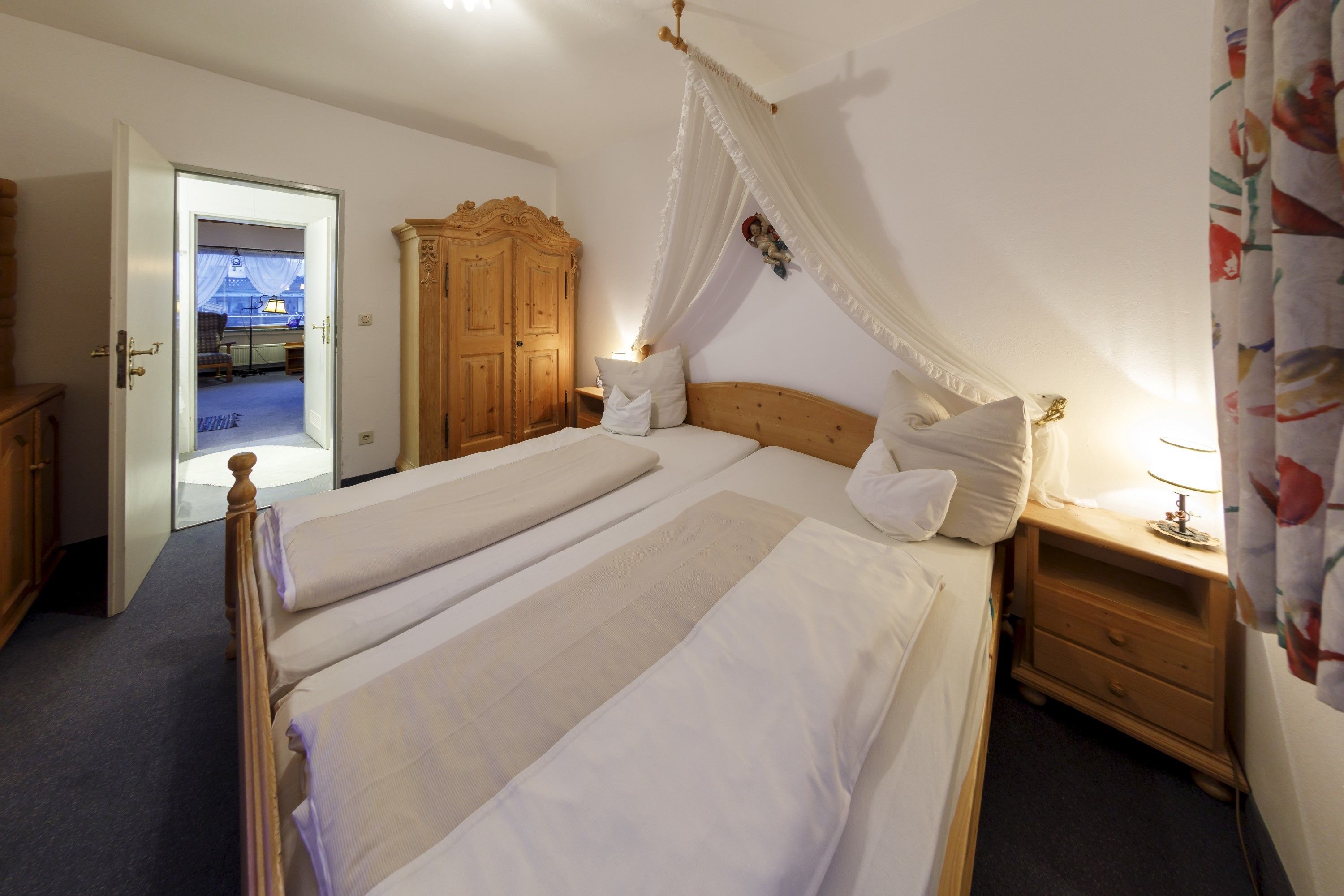 Ein Schlafzimmer mit zwei Einzelbetten, einem Holzschrank, einem Nachttisch mit Lampe und einem Himmelbett.