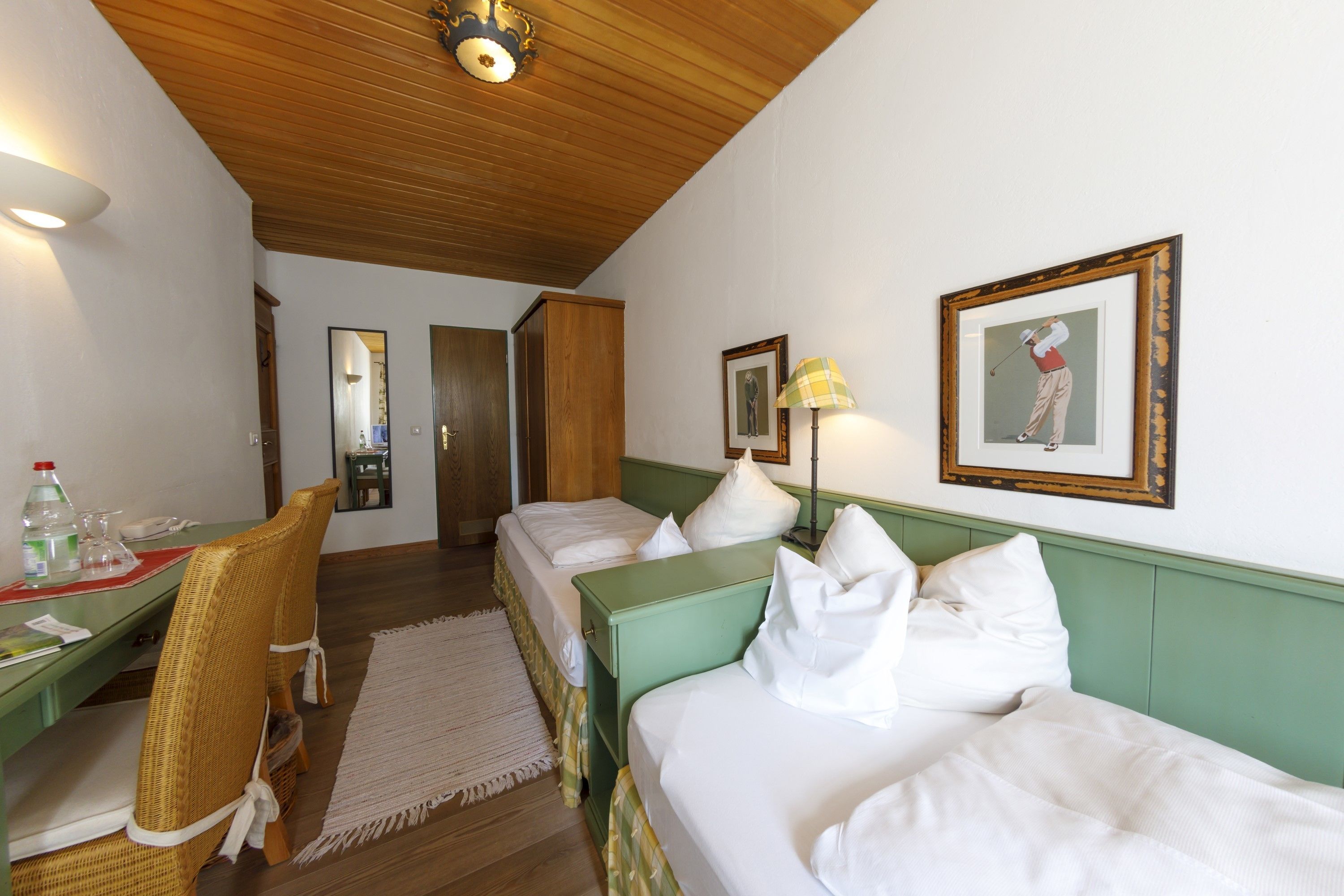 Hotellihuone, jossa on kaksi erillistä sänkyä, työpöytä tuolilla, peili ja seinällä oleva kehystetty kuva.