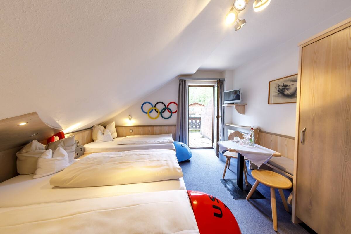 Een hotelkamer met drie bedden, een tafeltje, een stoel, een televisie en een deur.