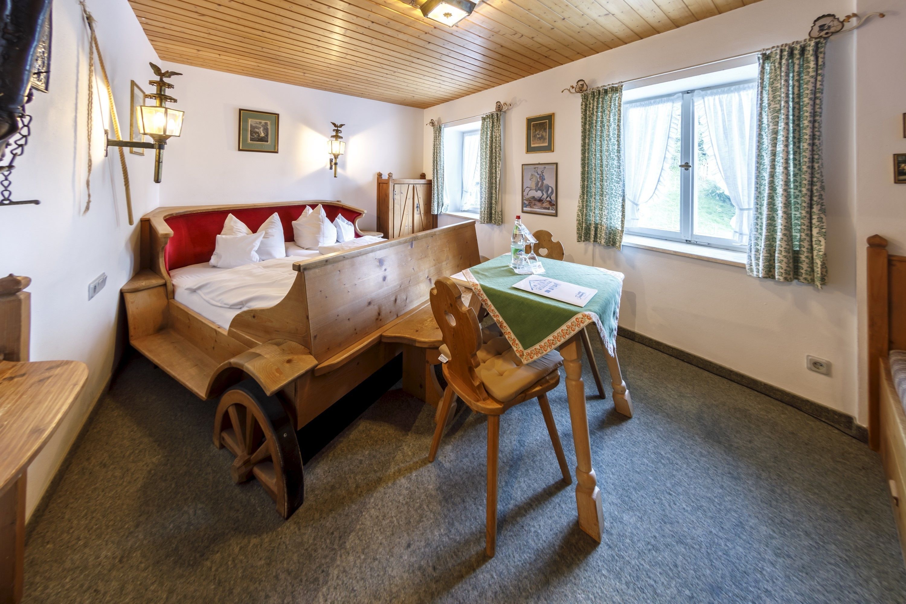 A traditional wooden bed with a red headboard, a wooden table with a green tablecloth, and a wooden chair.