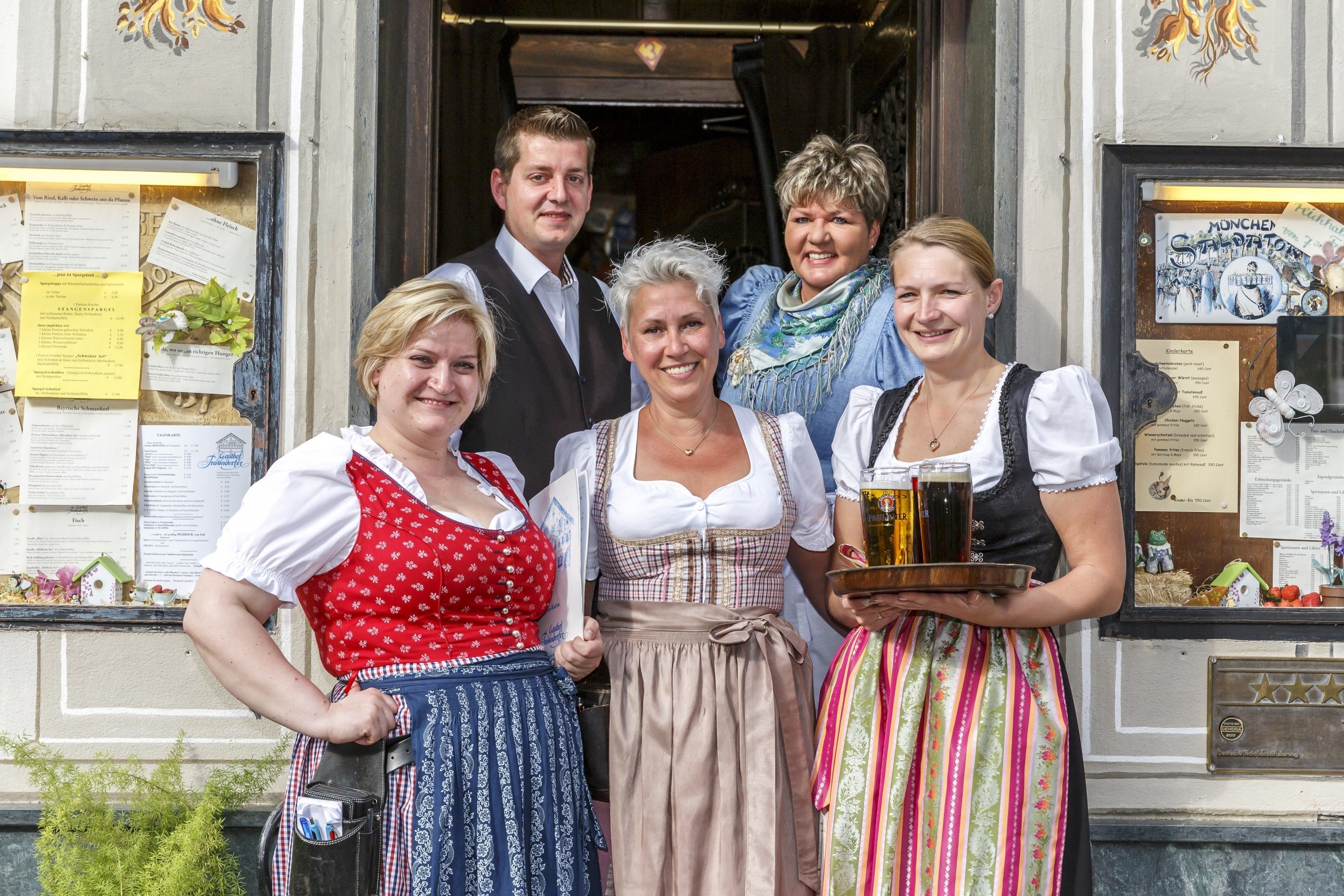 A group of people in traditional attire standing in front of a building with a menu board visible.
